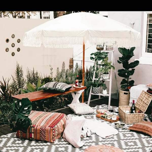 Bohemian outdoor patio with a white umbrella, plants, and a picnic spread from PIK-NIK Deli.