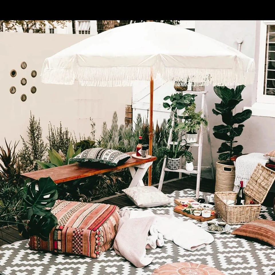 Bohemian outdoor patio with a white umbrella, plants, and a picnic spread from PIK-NIK Deli.