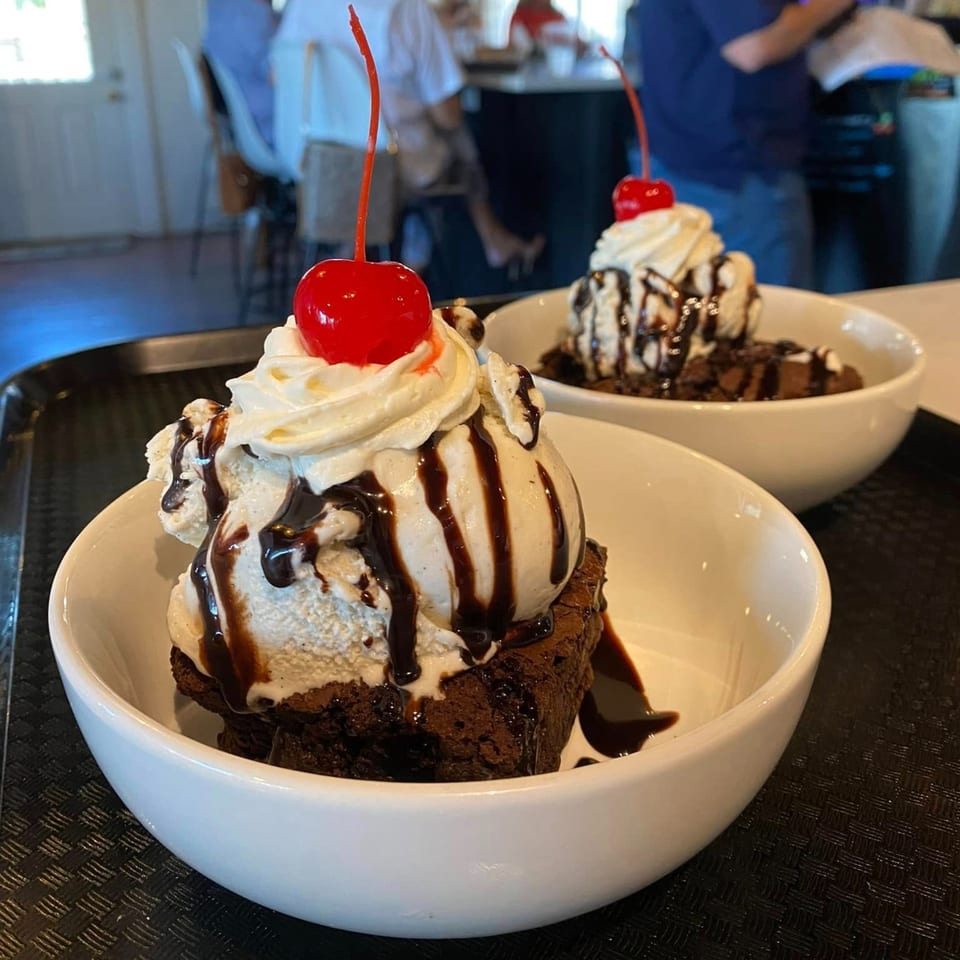 Two brownie sundaes with vanilla ice cream, chocolate syrup, whipped cream, and a cherry.