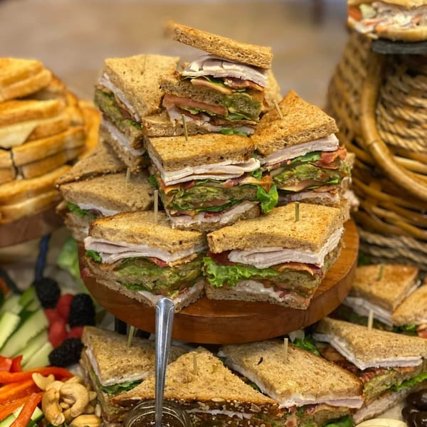 A tiered display of PIK-NIK Deli + Wine Bar's turkey and avocado club sandwiches, with a side of vegetables.
