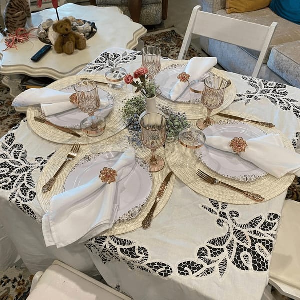 A dining table set with white plates, ornate gold cutlery, and floral napkin rings, ready for guests.