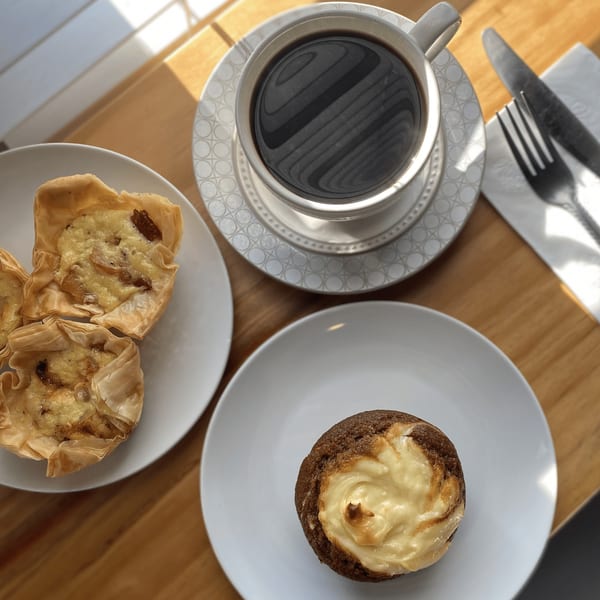 Overhead view of coffee, two phyllo pastries, and a cream cheese muffin on a wooden table.