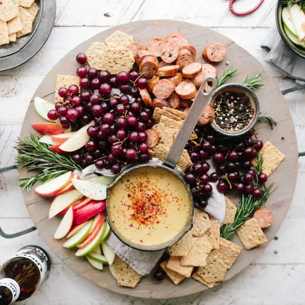 A PIK-NIK Deli + Wine Bar charcuterie board with cheese fondue, sausage, grapes, apples, and crackers.