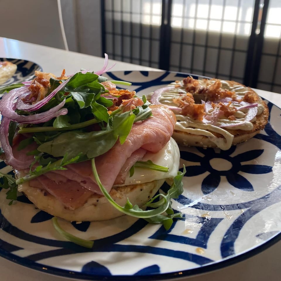 Two bagels from PIK-NIK Deli, one with ham, arugula, and red onion, on a blue and white plate.