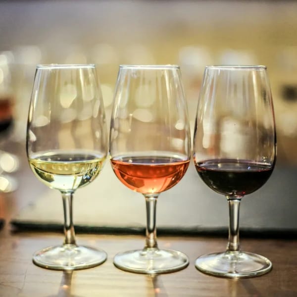 Three wine glasses on a table, filled with white, rosé, and red wine.