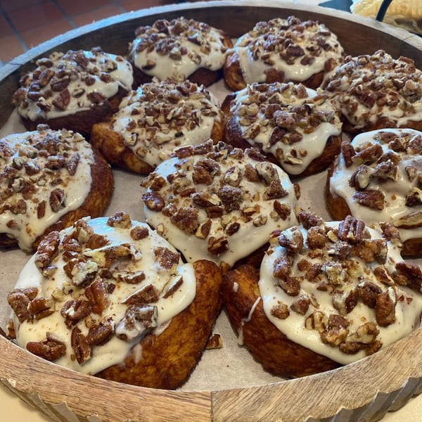 A wooden tray filled with freshly baked cinnamon rolls topped with white icing and chopped pecans.