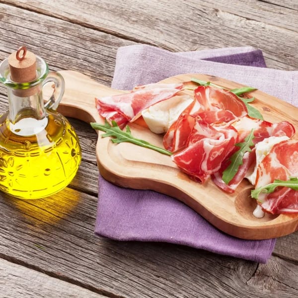 Cured meats and mozzarella with arugula on a wooden board, with olive oil on a rustic table.