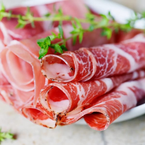 Close-up of thinly sliced, rolled deli meats with fresh herbs on a white plate.