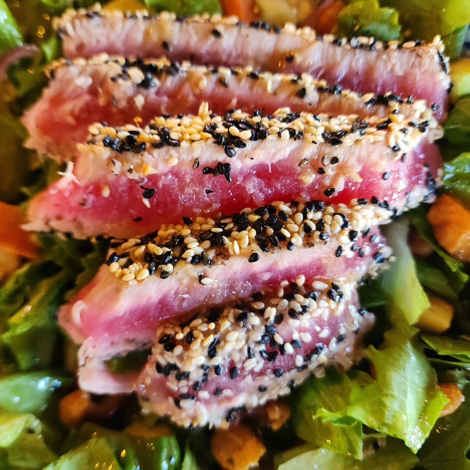 Close-up of seared tuna slices with sesame seeds on a bed of fresh green salad.