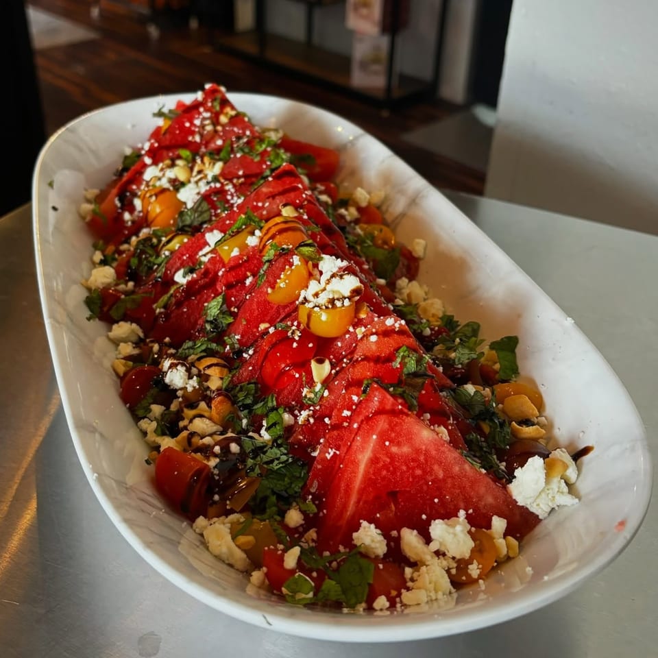 Watermelon salad with feta, cherry tomatoes, mint, and balsamic glaze in a white dish.