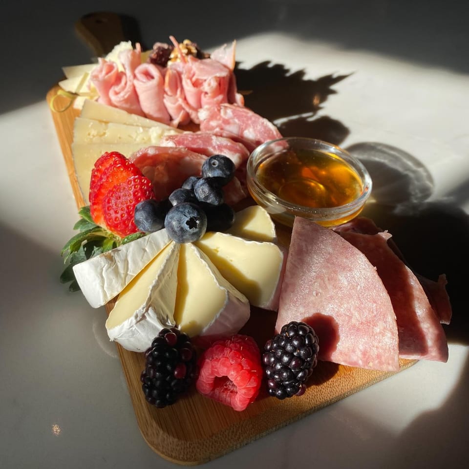 A PIK-NIK Deli + Wine Bar charcuterie board with meats, cheeses, berries, and honey.